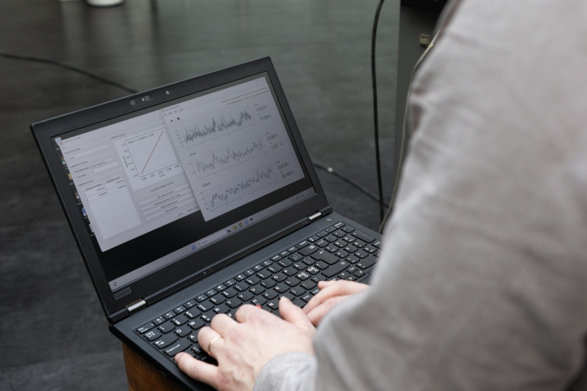 Person operating a laptop running Tapio Measurement software, with signal plots and calibration interface visible on the screen.
