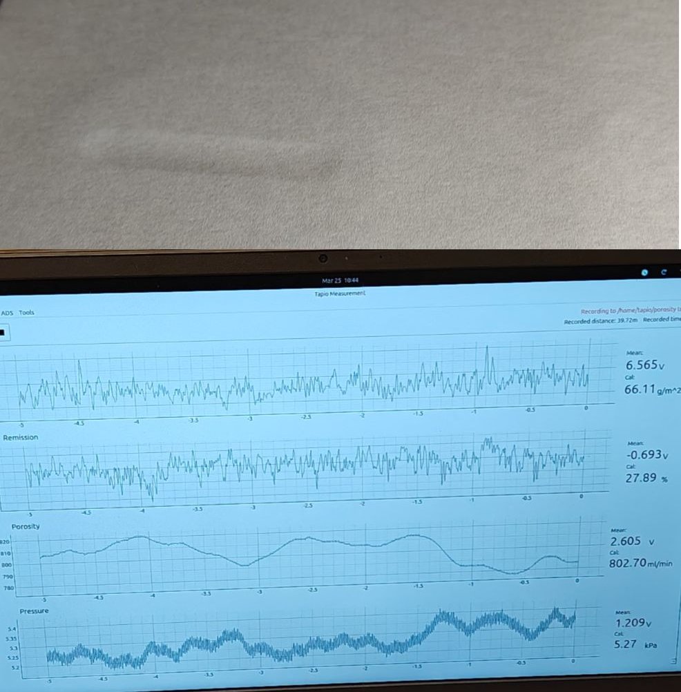 Paper sheet on a measurement device with a screen displaying porosity, pressure and signal graphs.